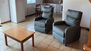 A living room with a wooden ceiling, a dining area with a table and chairs, and a kitchen in the background. - The stable, quiet house in the countryside (Quéménéven)