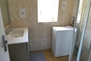 Un baño pequeño con lavamanos, espejo, ventana y una lavadora blanca.