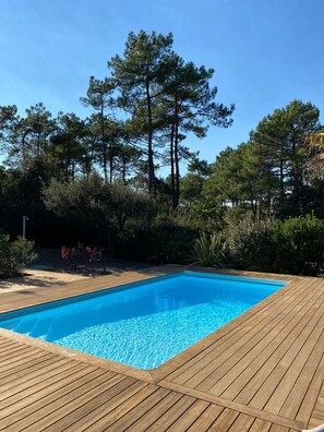Une piscine rectangulaire à l’eau d’un bleu cristallin, entourée d’une terrasse en bois.