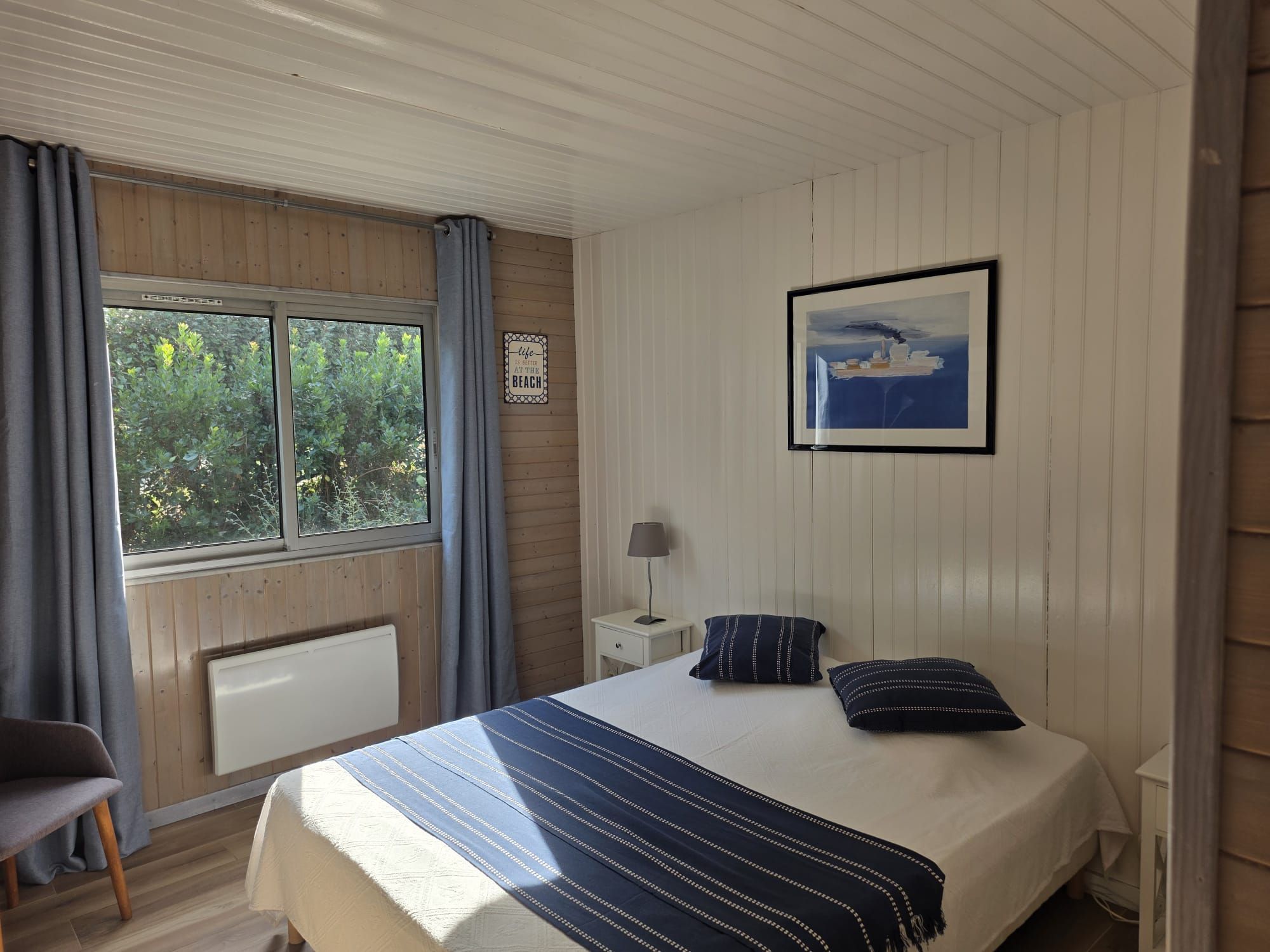 A bedroom with a bed, a nightstand, a lamp, a chair, and a window with curtains.