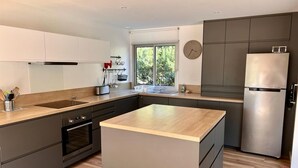 A modern kitchen with a central island, dark cabinetry, and a stainless steel refrigerator.