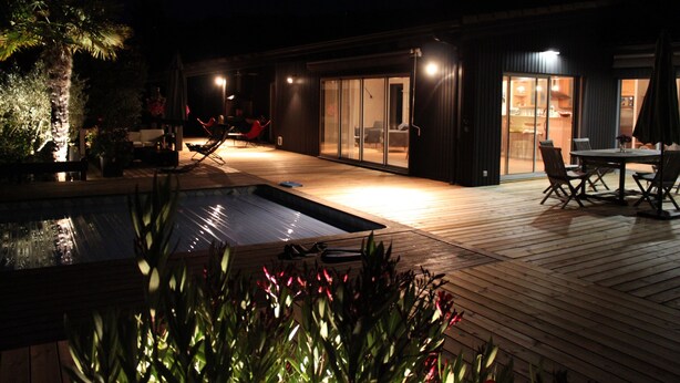 A modern outdoor patio area with a pool, wooden deck, and seating arrangements.