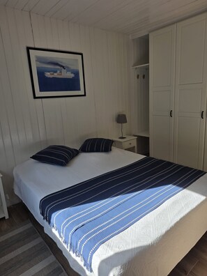 Une chambre à coucher avec un lit, des oreillers, une table de chevet, une lampe et une armoire.