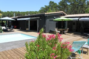 Un espace aménagé au bord de la piscine, avec une terrasse en bois, des chaises longues et des parasols.