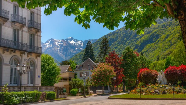 Ein Hotel mit Bergblick, ein Garten mit roten Blumen und eine Statue.