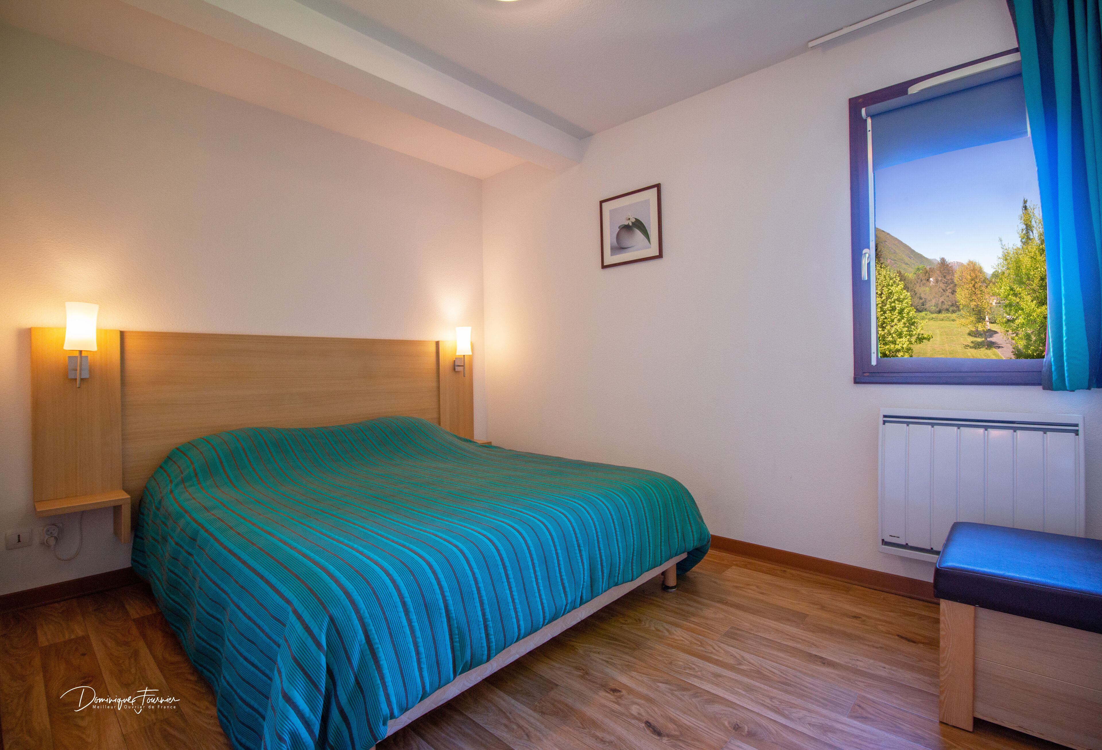Een slaapkamer met een bed, bedlampen, een raam met uitzicht en een radiator.