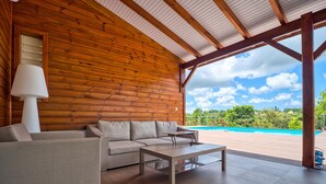 Une cabane en bois avec un canapé et une table, une lampe, et une vue sur une piscine.