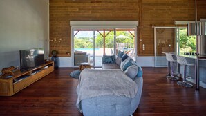 Un salon spacieux avec un grand canapé, un téléviseur et un ventilateur de plafond. Une porte-fenêtre coulissante donne accès à un espace extérieur comprenant une piscine et du mobilier de jardin.