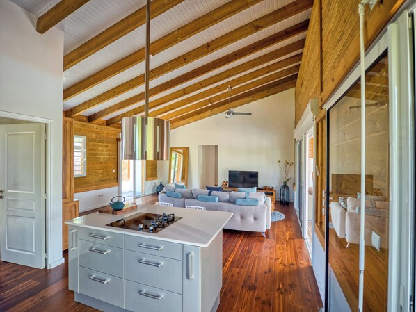 Een ruime woonkamer met een groot kookeiland, houten balken en een moderne keuken.