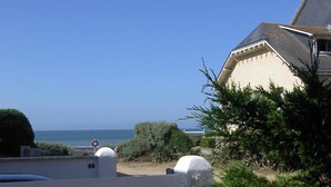 A coastal view with a clear sky, a white building with a grey roof, and a blue fence.