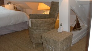 A hotel room with a bed, a wicker chair, a small table with a phone, and a lamp.