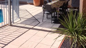 Un'area patio esterna con tavolo e sedie al coperto, una pianta in vaso e una piscina.