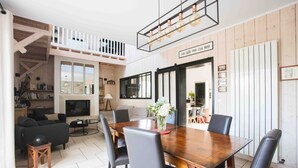 Un coin repas avec une table en bois et des chaises noires, un canapé et un téléviseur en arrière-plan.