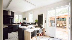 Une cuisine moderne dotée d’un îlot central, de meubles de rangement noirs et d’une grande porte-fenêtre coulissante donnant sur une terrasse extérieure.