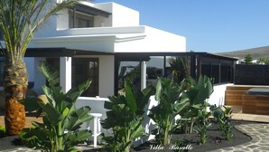 Une villa moderne dotée d’un patio, entourée de plantes tropicales et présentant une façade blanche.