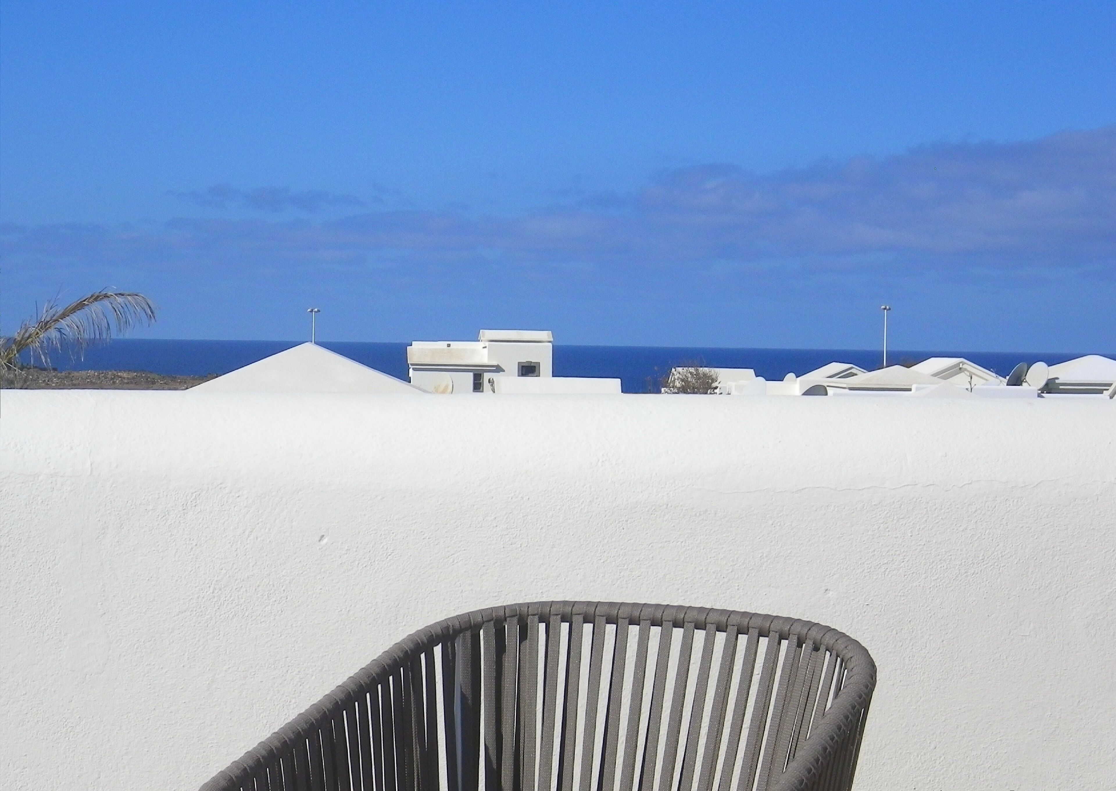 A white building with a flat roof, a clear blue sky, and the sea in the background.