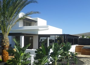 A modern villa with a patio area, surrounded by tropical plants and a white exterior.