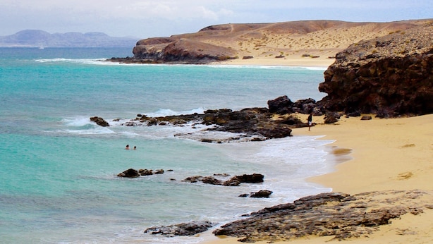 Un paysage côtier caractérisé par une eau turquoise et limpide, des falaises rocheuses et une plage de sable.
