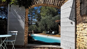 Una piscina al aire libre con un arco de piedra, rodeada de vegetación y un muro de piedra.