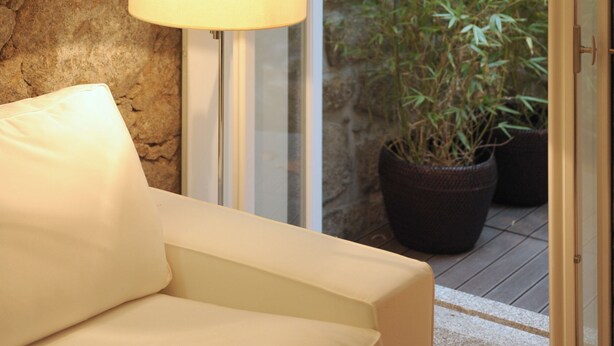 Ein Zimmer mit einer Steinsäule, einem weißen Sofa, einer Stehlampe und einer Glastür, die in einen Bambusgarten führt.