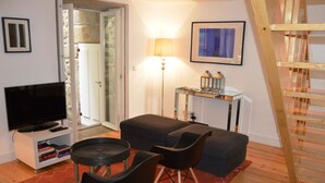 Ein Wohnzimmer mit Fernseher, einer Couch, Sesseln, einer Lampe und einer Holztreppe.