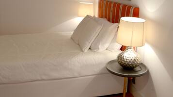 A neatly made bed with pillows, a bedside lamp, and a rug on a wooden floor.