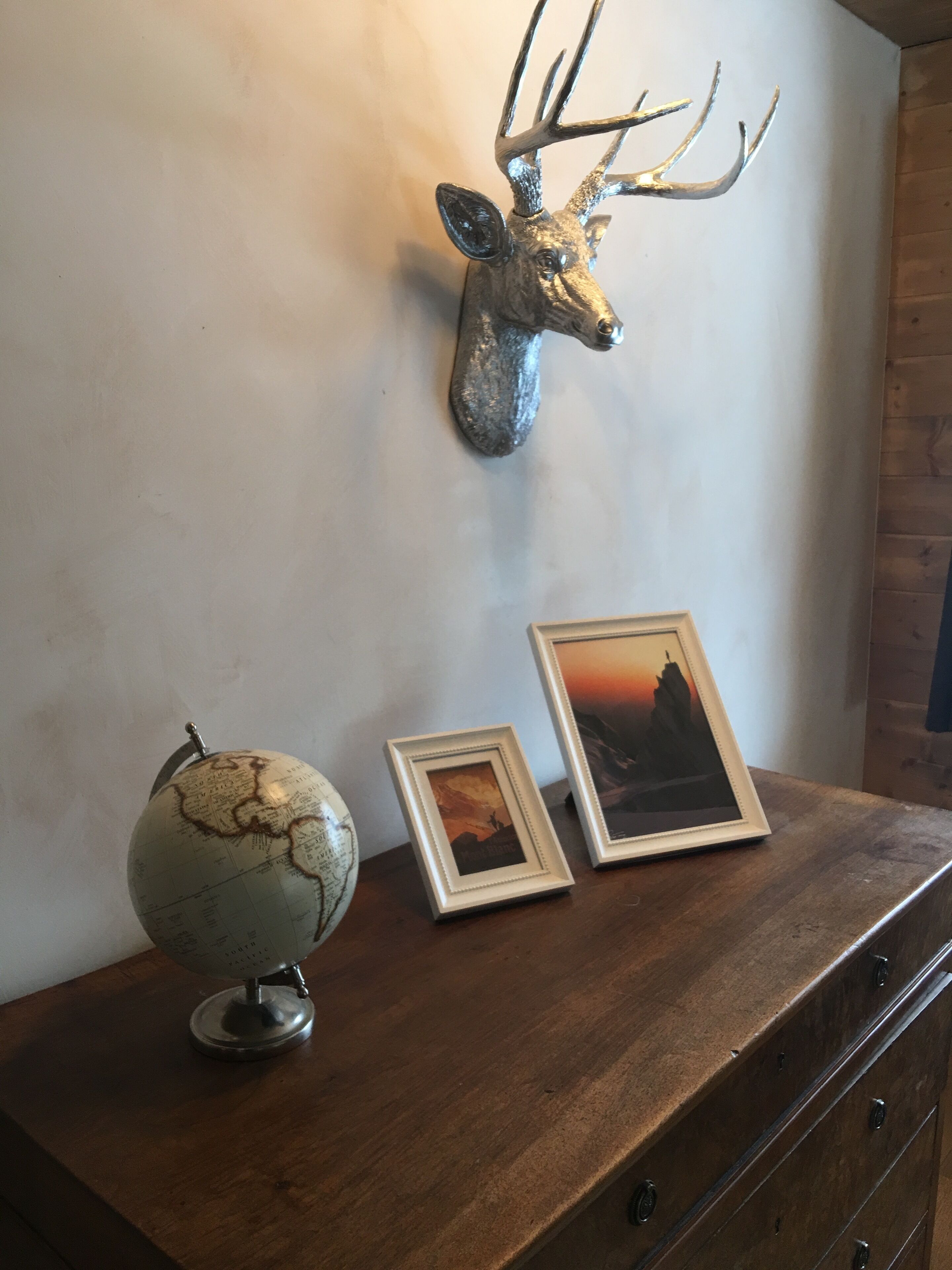 A wooden dresser with a mounted deer head, a globe, and two framed pictures.
