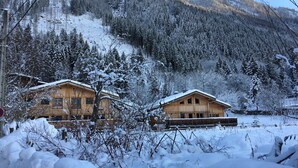 A wooden cabin with a snow-covered roof, surrounded by a forest and mountains. - 1/2 Chalet close to the center, quiet, private parking, 4 bedrooms 2 bathrooms (Chamonix-Mont-Blanc)