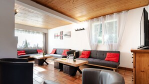Een moderne woonkamer met een houten plafond, twee banken met rode kussens, een salontafel en een televisie op een houten kast.