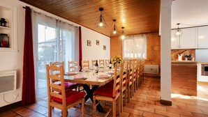 Een eetgedeelte met houten stoelen en een gedekte tafel, een keuken met een tegelwand en een raam met gordijnen.