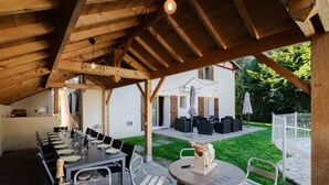 Een buiten eethoek met een lange tafel gedekt voor een maaltijd, omringd door stoelen en een houten pergola.