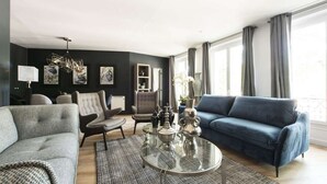Ein modernes Wohnzimmer mit einem grauen Sofa, einem blauen Sofa, einem Glastisch und einem gemusterten Teppich.