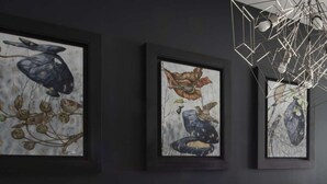 Ein Zimmer mit drei gerahmten Kunstwerken an der Wand, einer geometrischen Leuchte und einer kleinen Skulptur auf dem Tisch.
