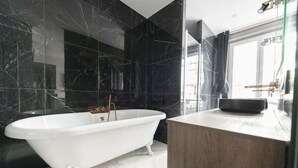 Ein modernes Badezimmer mit einer freistehenden Badewanne, Marmorwänden und einem Holzlaufschrank.