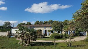 A stone house with a tiled roof, surrounded by a well-maintained garden and trees. - House, private pool near sea Charente-Maritime near La Rochelle, Cognac (Tonnay-Boutonne)