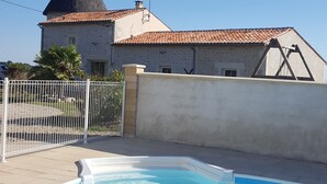 A swimming pool with a clear blue water surface, a white fence, and a building with a conical roof and a stone facade. - House, private pool near sea Charente-Maritime near La Rochelle, Cognac (Tonnay-Boutonne)