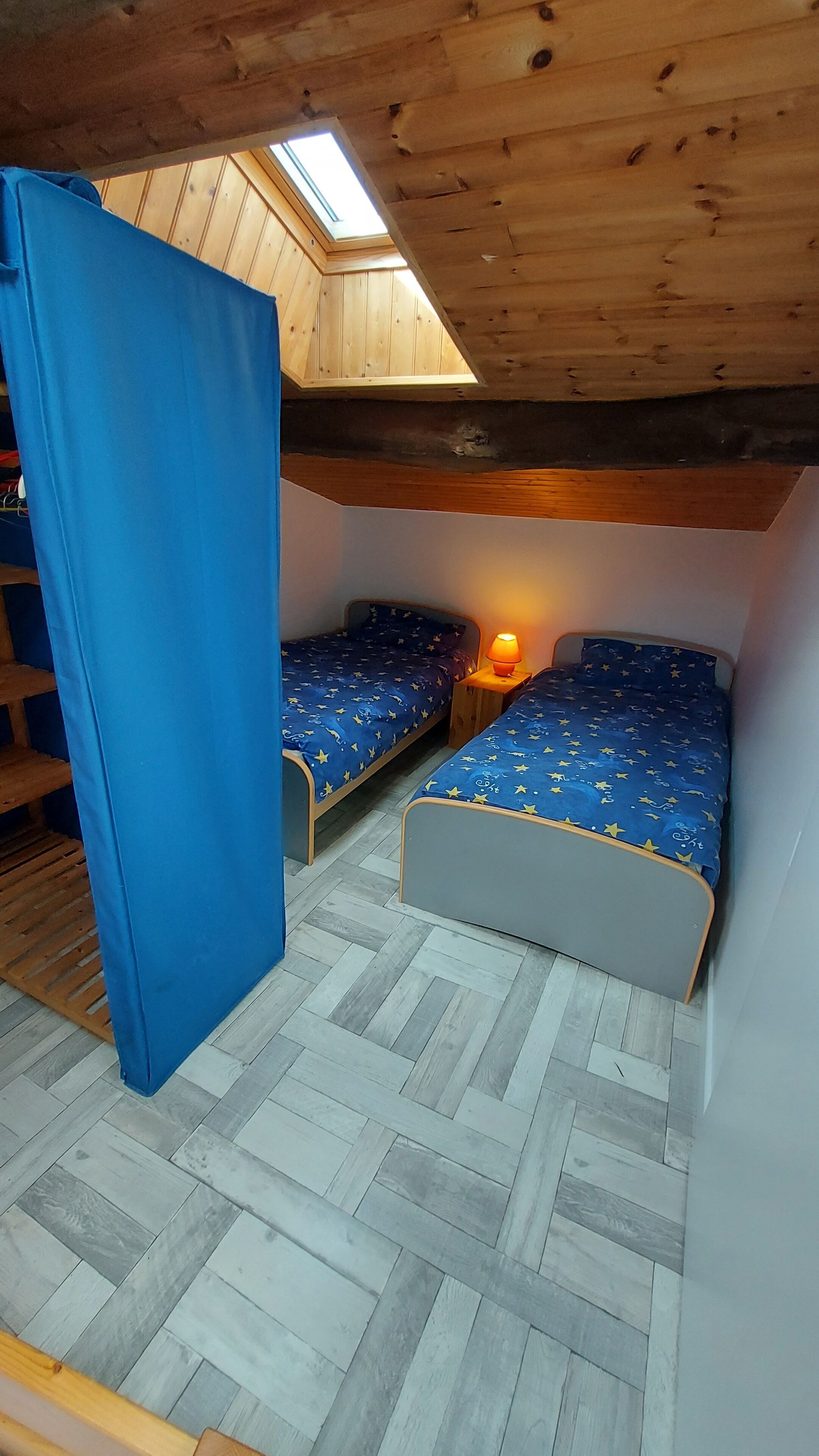 Una habitación pequeña y acogedora con dos camas, un tragaluz y techo de madera.