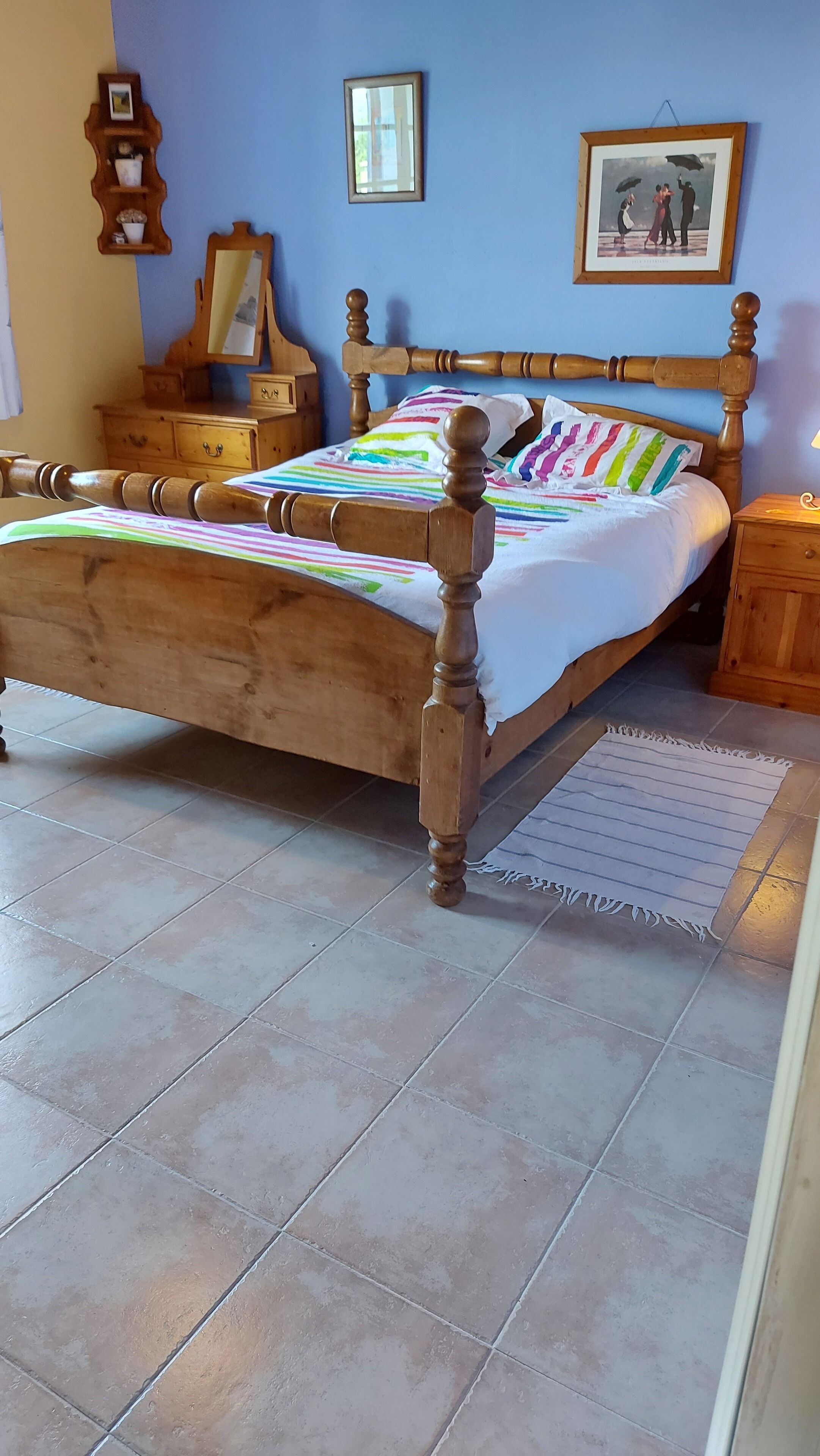 A bedroom with a wooden bed, a nightstand, a dresser, and a wall-mounted shelf.