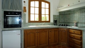A kitchen with wooden cabinets, a built-in oven, a sink, and a window with a curtain. - Holiday villa with pool Les Vignes - bastides-du-luberon.com (La Tour-D'aigues)