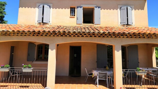 A two-story building with a tiled roof, multiple windows with shutters, and a covered patio area with tables and chairs. - Holiday villa with pool Les Vignes - bastides-du-luberon.com (La Tour-D'aigues)
