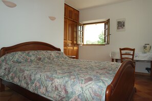 A bedroom with a bed, wooden wardrobe, open window, chair, and table with a vase.