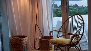 A modern living room with a large window, wicker baskets, a wicker chair, a small table with a candle, and a red floor lamp. - Villa with an exceptional view of the sea and the bay of Agay (Saint-Raphaël)