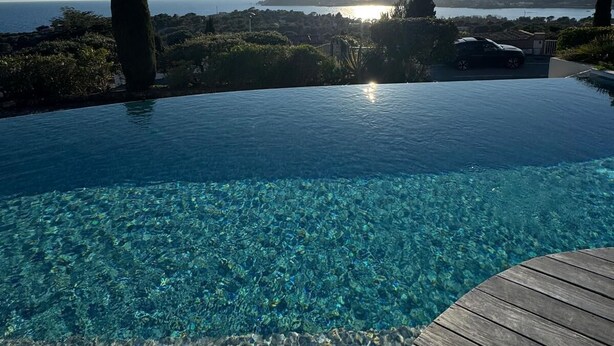 An infinity pool with clear water, a wooden deck, and a view of the sea and distant hills. - Villa with an exceptional view of the sea and the bay of Agay (Saint-Raphaël)