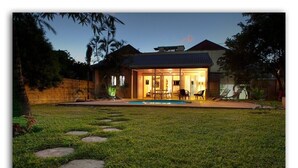 A house with a swimming pool, a covered patio, and a well-maintained lawn with stepping stones.