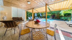 A covered patio area with a round table and chairs, a pool, and outdoor seating.