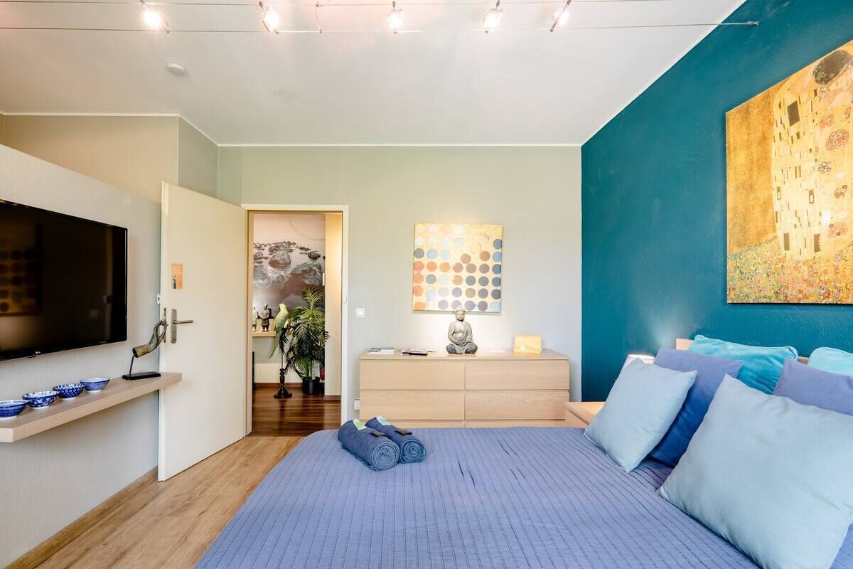 Un dormitorio moderno con una cama grande, un televisor de pantalla plana, un aparador de madera y un cuadro en la pared.