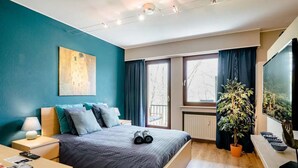 Un dormitorio moderno con cama, mesita de noche, lámpara y un ventanal con cortinas.