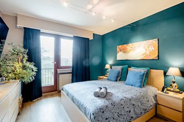 Une chambre à coucher comprenant un lit, deux tables de chevet, une commode, une plante en pot et une fenêtre avec des rideaux.