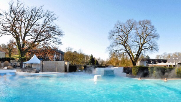 Una piscina con agua azul cristalina, rodeada de árboles y edificios.