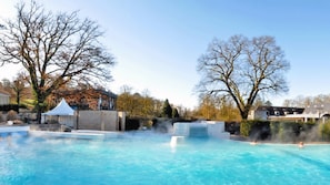 Une piscine à l’eau d’un bleu limpide, entourée d’arbres et de bâtiments.